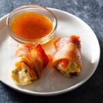 Two bacon-wrapped stuffed shrimp with sauce on a plate.