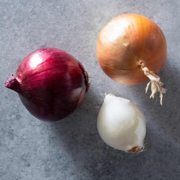 A yellow, a red and a white onion on a table.