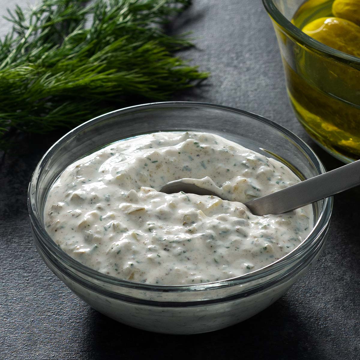 Sour cream tartar sauce in a glass bowl with a small spoon.