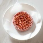 A seasoned frozen hamburger patty on a plate.