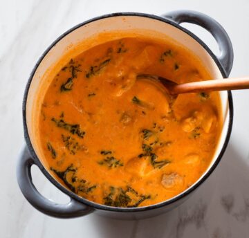 Creamy chorizo soup being stirred in a Dutch oven.