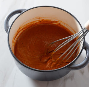 Creamy red enchilada sauce being whisked in a pot.