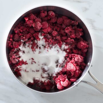 Frozen raspberries and sugar in a saucepan.