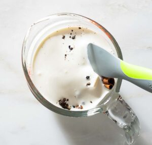 Spices and cream being stirred in a liquid measuring cup.