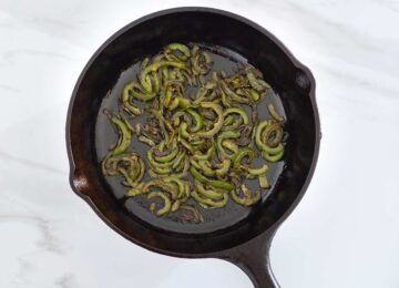 Charred jalapeno pepper slices in a cast iron pan.