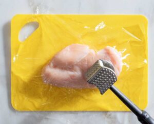 Raw chicken breast and meat mallet.