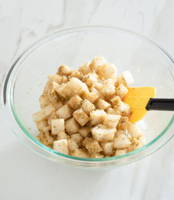 Bread cubes being tossed in a bowl.