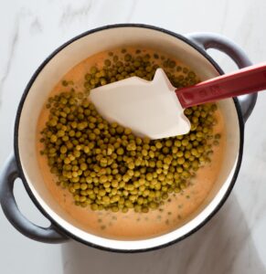 Creamed canned peas in a pot with a spatula.