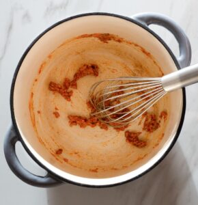 Roux with spices being whisked in a pot.