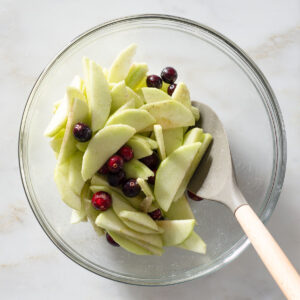 Apple slices and cranberries being mixed in a bowl.